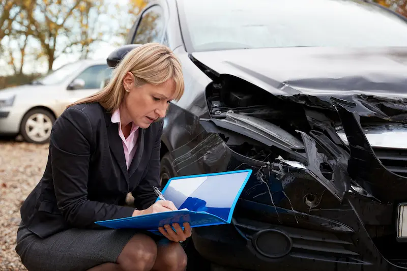 An insurance adjuster reviews damage to a vehicle involved in a car accident.