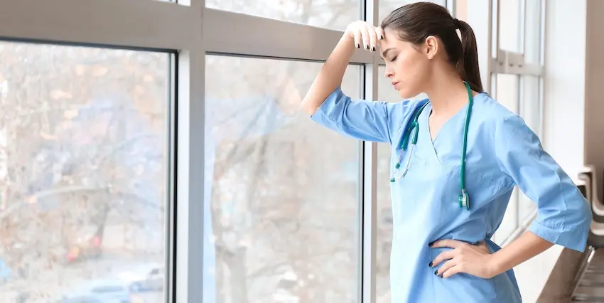 An exhausted healthcare worker in blue scrubs is standing by a hospital window reflecting on a wrongful death medical malpractice case in South Carolina.