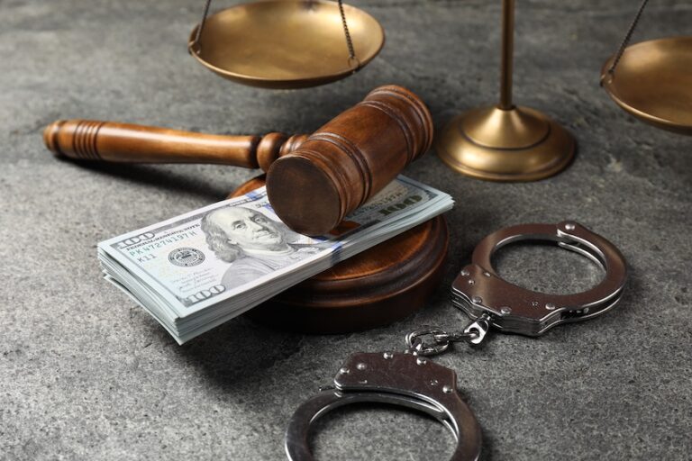Judge's gavel resting on a stack of cash with handcuffs and scales of justice symbolizing wrongful death lawsuit compensation at McDougall LawFirm, LLC.