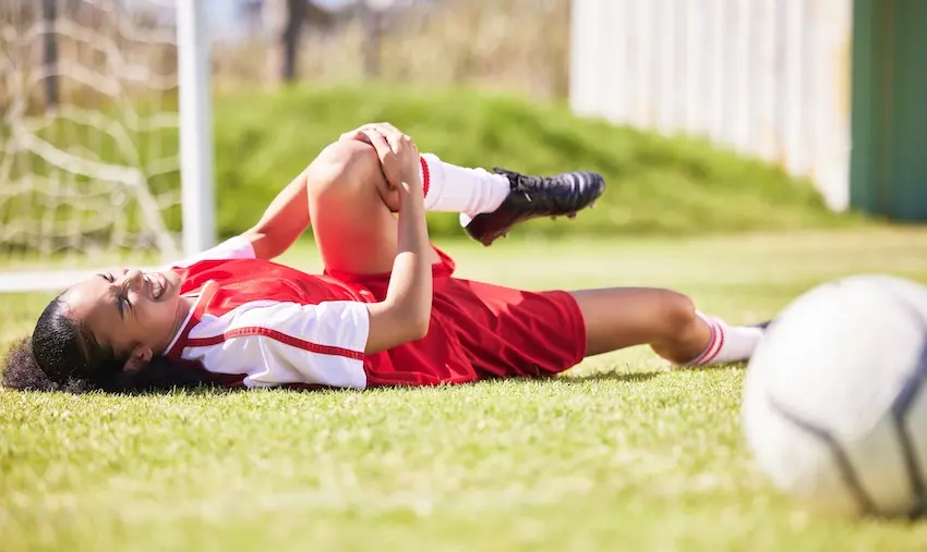 A young female soccer player is lying on the field with a knee injury requiring consultation with a sports injury attorney from McDougall LawFirm LLC in South Carolina.