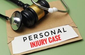 A black and gold judge's gavel with a white rubber tip sits atop a torn brown kraft paper envelope alongside a silver and black stethoscope- all arranged on a sage green surface- with a white rectangular label beneath the gavel printed with the words "PERSONAL" in bold black letters and "INJURY CASE" in bold red letters — directly referencing the legal and medical documentation central to a personal injury case in South Carolina.