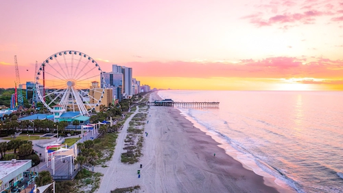 sunrise over a beach with a ferris wheel and pier